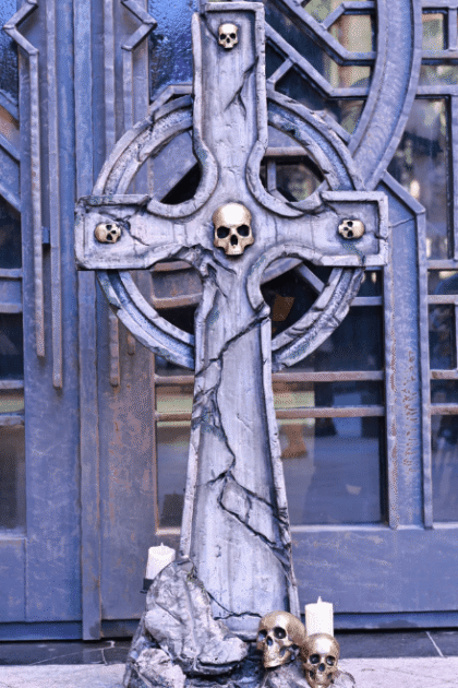 Front view of the Gothic Warrior Memorial Cross cosplay prop with lights off, showing 3D printed skeleton heads, figures, and plastic candles on a styrofoam cross.